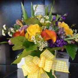 Mixed bouquet with yellow roses, orange calla lilies, and purple flowers in a vase