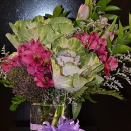 Pink alstroemeria and green ornamental cabbage in a glass vase with a purple ribbon.