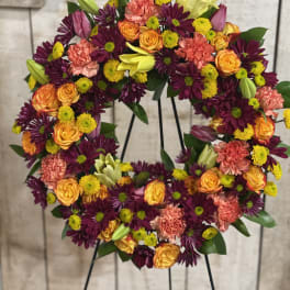 Floral wreath on a stand with orange roses, purple daisies, and pink carnations