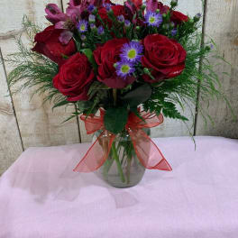 Bouquet of red roses and purple flowers in a glass vase with a red ribbon