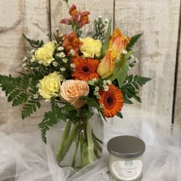 Mixed bouquet in a glass vase beside a scented candle