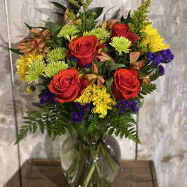 Mixed bouquet of red roses, yellow chrysanthemums, and purple filler in a glass vase