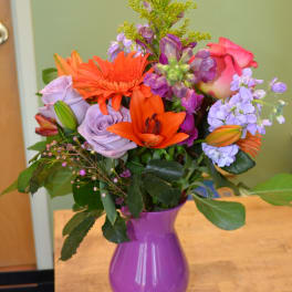 Mixed bouquet of orange, pink, and lavender flowers in a purple vase
