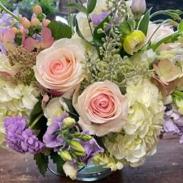 Bouquet of pale pink roses, white hydrangeas, and lavender flowers in a glass vase