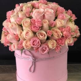 Pink and cream roses arranged in a round pink hat box