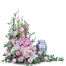 Pink lilies and roses arranged beside a silver cremation urn.