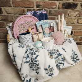 Gift basket with candles, bath items, and accessories on a floral blanket