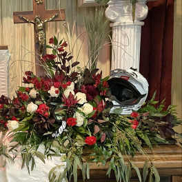 Red and white floral casket spray with roses and carnations displayed beside a white motocross helmet.