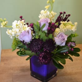 Lavender roses and white flowers in a purple glass vase