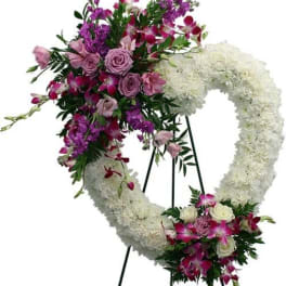 Heart-shaped white sympathy wreath with purple and pink flowers on a standing easel