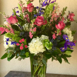 Tall mixed bouquet of pink roses, purple irises, and white hydrangeas in a glass vase