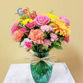 Colorful bouquet in a green glass vase with a "Get Well" sign