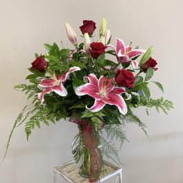 Tall vase arrangement of red roses and pink lilies with a red ribbon bow.