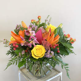 Bright arrangement of yellow roses, orange lilies, and pink blooms in a round clear glass vase