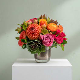 Mixed bouquet of orange, pink, and red flowers in a glass vase