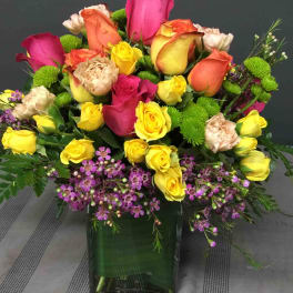 Mixed roses in a square glass vase with purple filler flowers