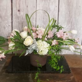 Low floral arrangement with white roses, pink blooms, and long white tulips in a brown pot