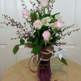 Pink roses and white lilies in a purple vase with ribbon