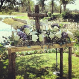 White and purple floral arrangements on a rustic wooden cross display