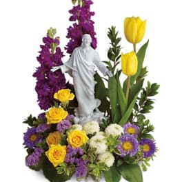 Floral arrangement with a white statue centerpiece, yellow tulips, roses, and purple flowers
