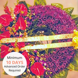 Large purple floral sympathy wreath with red tropical blooms, gold ribbon accents, and a message banner on a stand