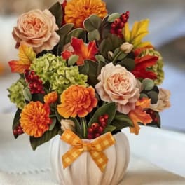 Fall floral arrangement in a white pumpkin container with an orange ribbon