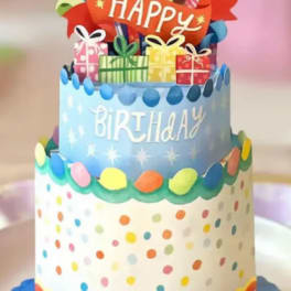 Decorated birthday cake with colorful gifts and a "Happy Birthday" topper