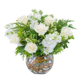 Low arrangement of white roses and stock in a clear glass bowl vase with curly branches in the water