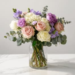 Glass vase bouquet of white, blush, and lavender roses with soft accent blooms