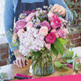 Round bouquet of pink and purple flowers in a clear glass vase on a table