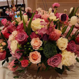 Low centerpiece of pink, purple, peach, and white roses with tulips and mixed blooms in a round bowl vase.