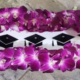 Purple orchid lei arranged around a white insert decorated with black graduation caps