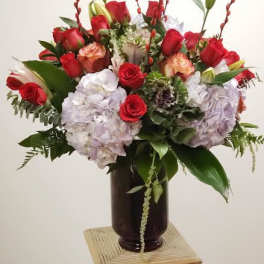Red roses and pale hydrangeas arranged in a dark vase