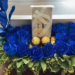 Blue roses arranged around a gift box and chocolates