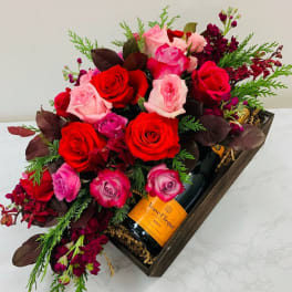 Red and pink roses arranged in a gift box with a champagne bottle