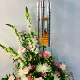 Standing floral arrangement with pink and white flowers beneath silver wind chimes