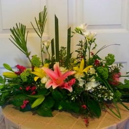 Low floral centerpiece with lilies and mixed blooms in a shallow container