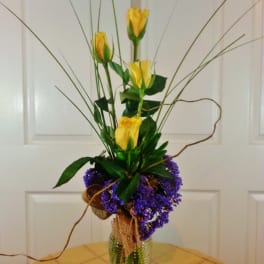 Tall arrangement of yellow roses in a glass vase with purple filler flowers
