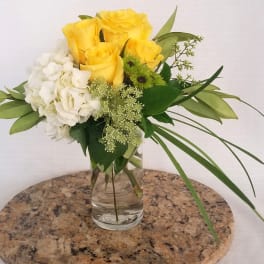 Yellow roses and white hydrangea in a clear glass vase