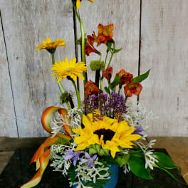 Mixed floral arrangement with yellow gerberas and sunflowers in a blue vase