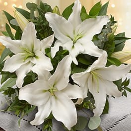 White lily bouquet with green foliage on a gray cloth