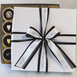 Gift box with black ribbon over a tray of assorted chocolates