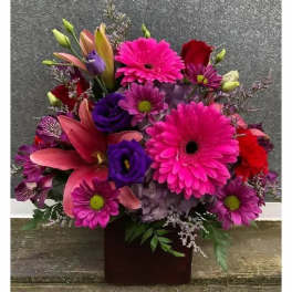 Bright mixed bouquet with pink gerberas, lilies, and purple blooms in a dark vase