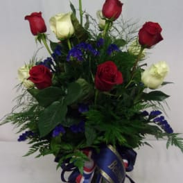 Red and white roses arranged in a glass vase with blue filler flowers.