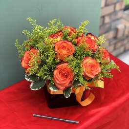 Orange roses in a black box with green filler and an orange ribbon