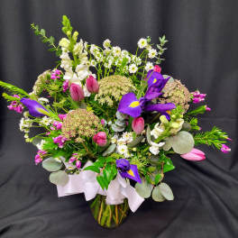 Mixed bouquet with purple irises, pink tulips, and white snapdragons in a glass vase