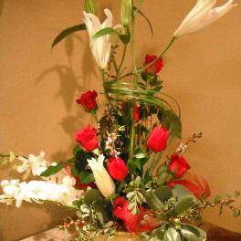 Tall floral arrangement with red roses and white lilies in a white vase
