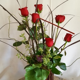 Tall arrangement of red roses in a woven basket with decorative branches