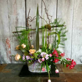 Tall floral arrangement with peach, pink, red, and purple blooms in a white container