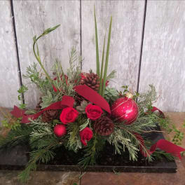 Red roses and pinecones arranged with holiday greenery and a red ornament
